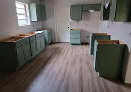 Empty kitchen with green cabinets, wood-look flooring, and a window on the left.