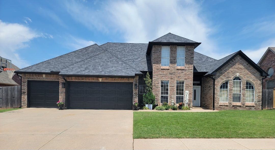 Brick suburban house with three-car garage, stone accents, and a front lawn under a blue sky