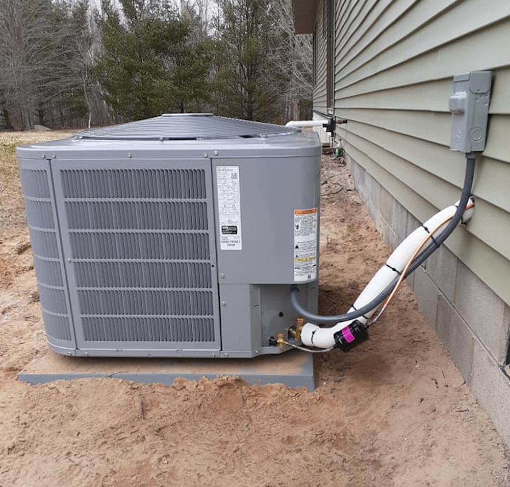 A gray air conditioner is sitting on the side of a house.