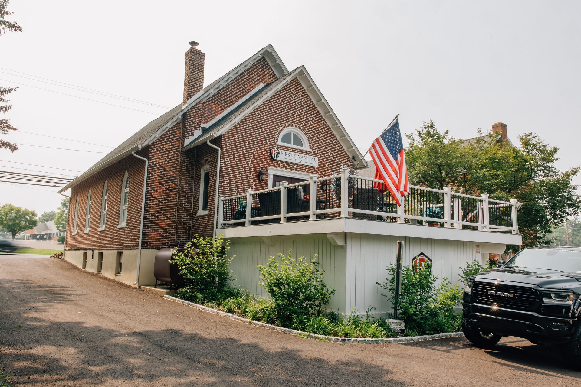 Brick building with American flag, white deck, and a black vehicle parked in front.