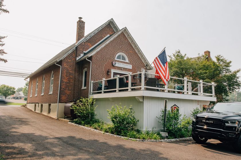 Brick building with American flag, white deck, and a black vehicle parked in front.
