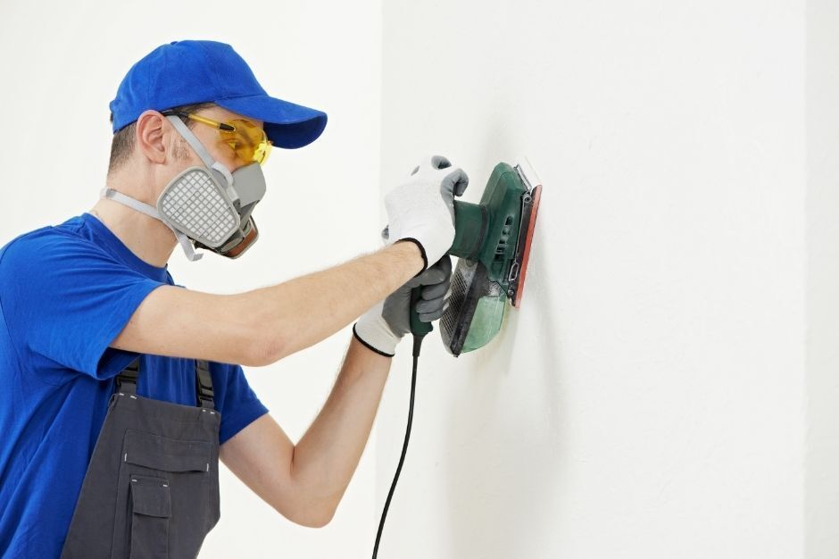 handyman sanding and painting a wall