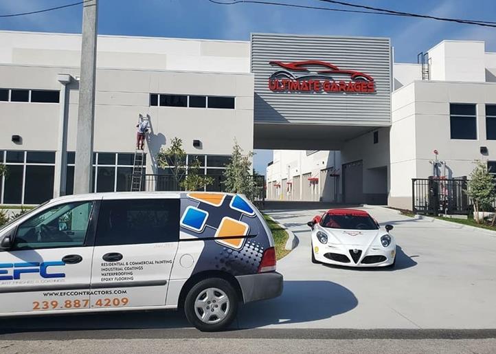 Exterior of an automotive business, with a white van, red sports car, and building with a logo.
