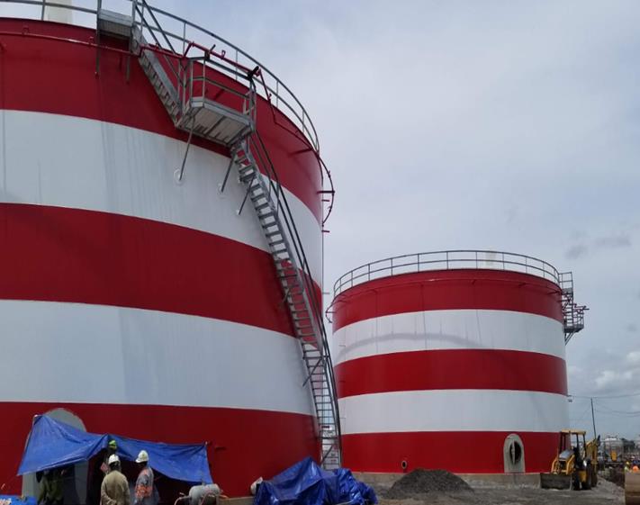 Two large, striped red and white storage tanks with metal ladders, on a construction site under a cloudy sky.