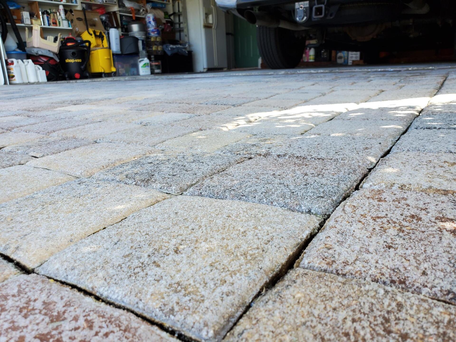 Close-up of a brick driveway, showing the surface's texture and seams, with a garage in the background.