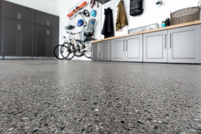 Gray speckled epoxy garage floor, cabinets, bikes, and storage on the wall.