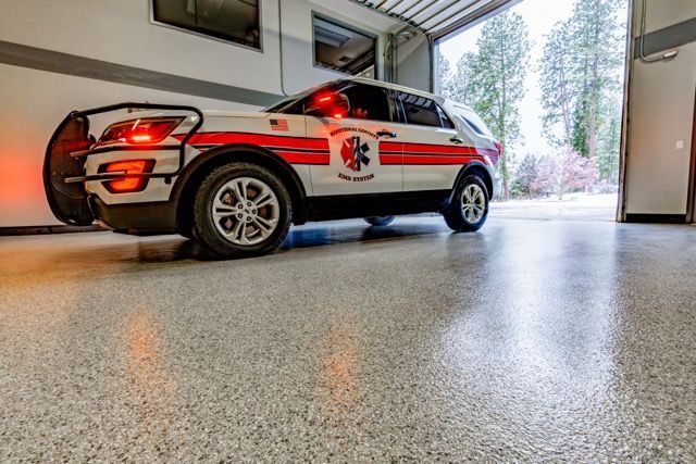Emergency vehicle in garage with lights on; white, red and silver paint; shiny, speckled floor.