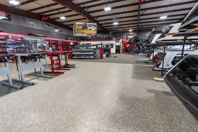 A large warehouse interior with vehicles, parts, and equipment. Concrete floor. Red and black accents.
