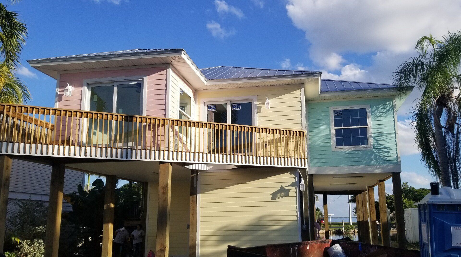 Two-story house on stilts; colorful exterior, wooden deck, blue sky.