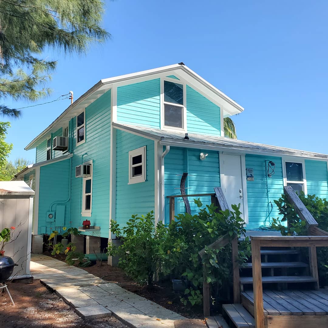 Turquoise two-story house with white trim and a small porch; sunny day.