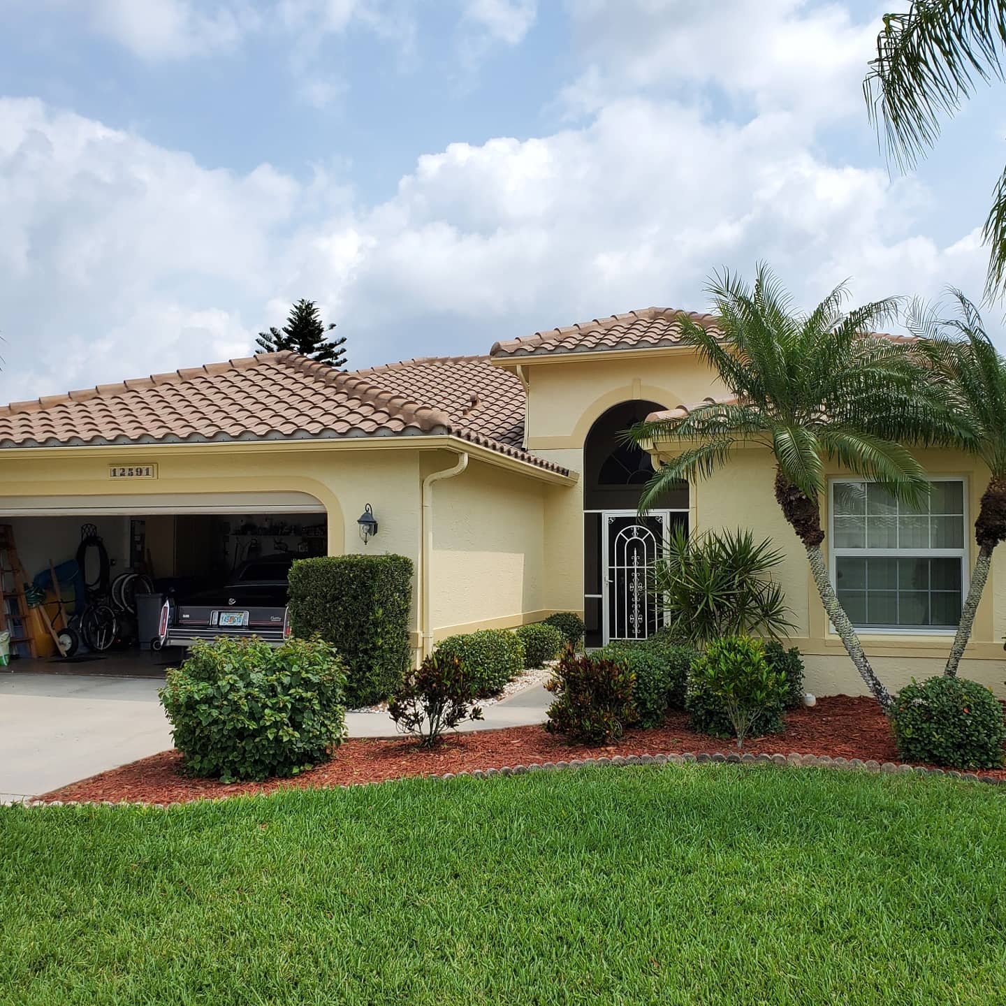 Yellow house with brown tile roof and green landscaping, with a car in open garage.