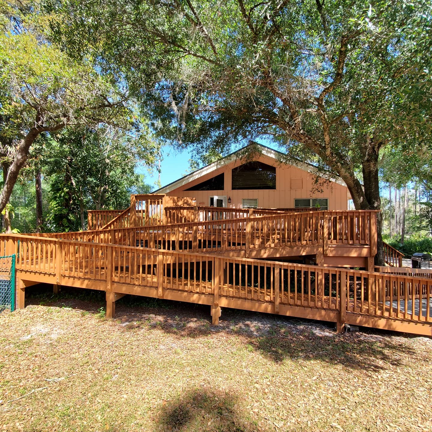 Brown wooden ramp leading to a peach-colored house, set among trees.