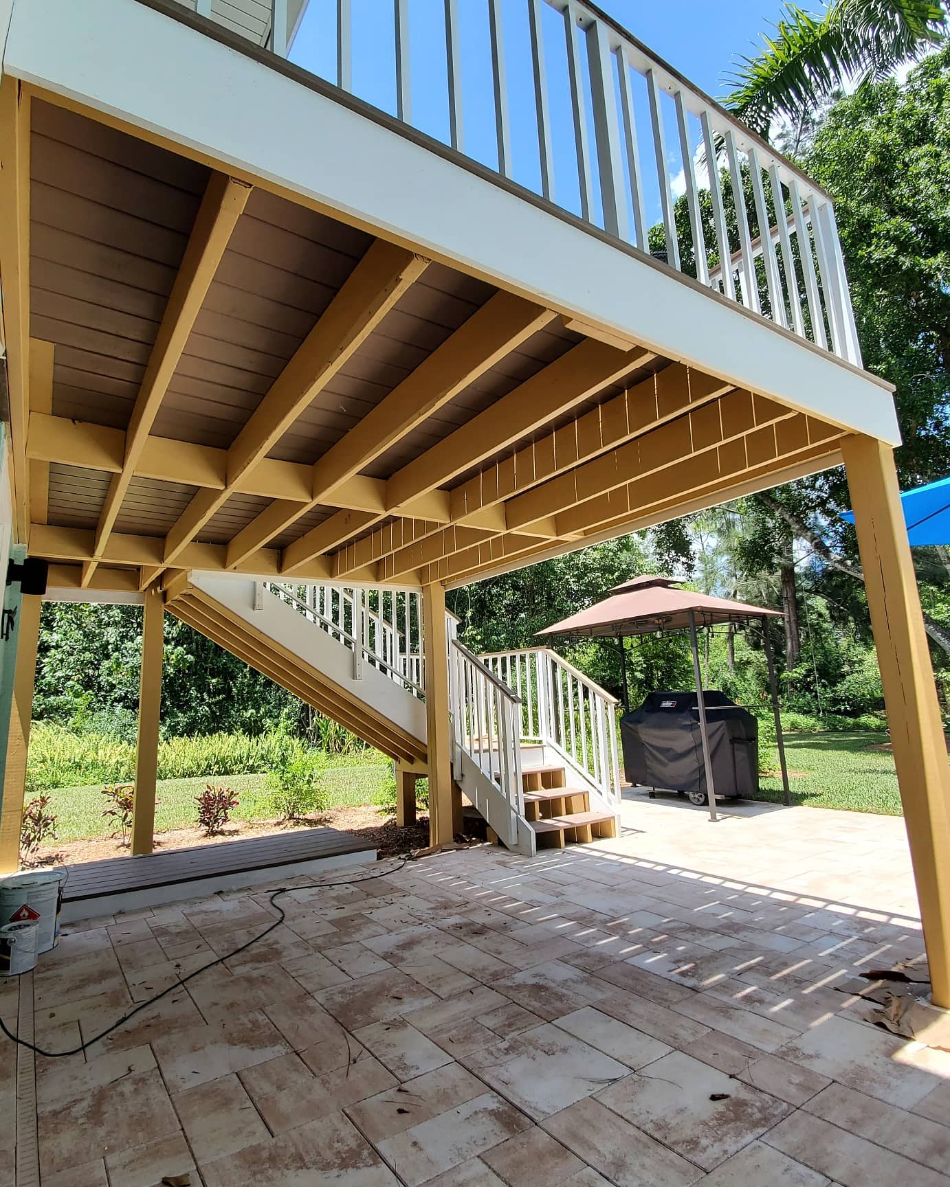View of a deck with stairs, supported by wood beams, over a stone patio.