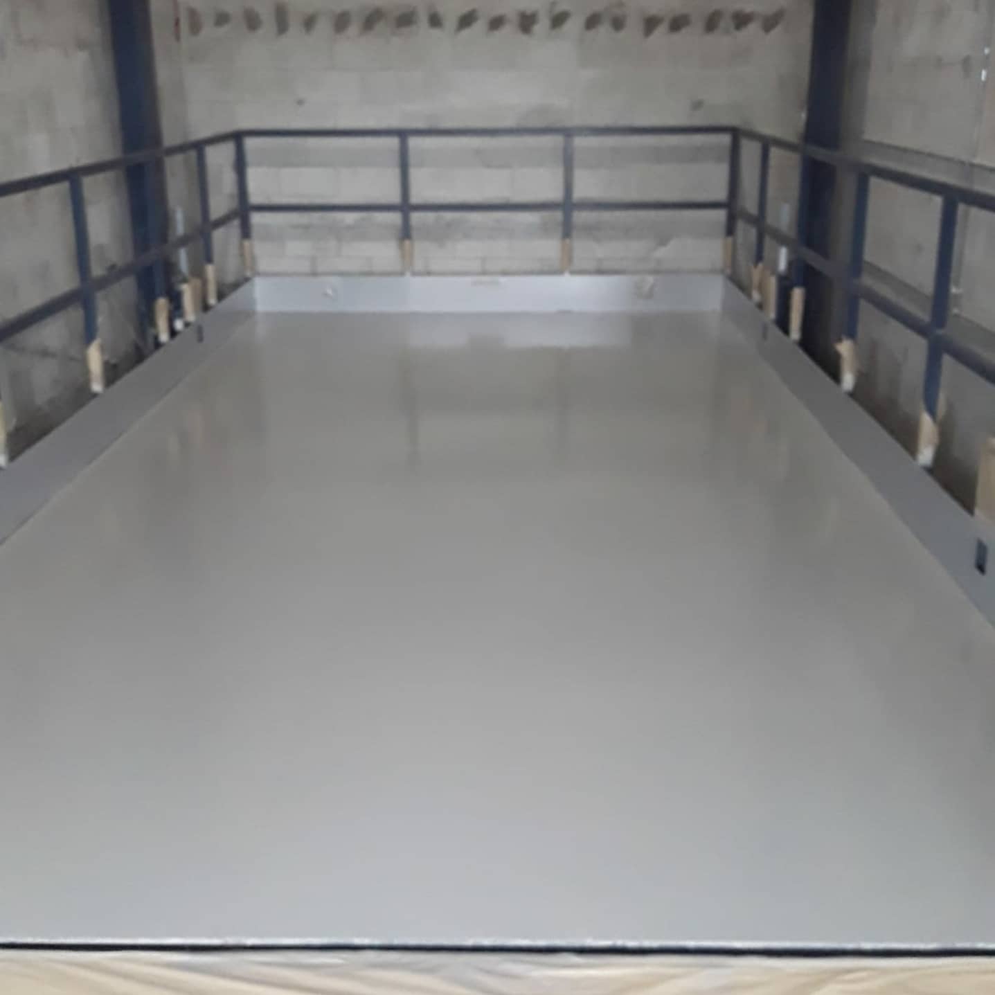 Gray-floored industrial platform with metal railing, inside a building.