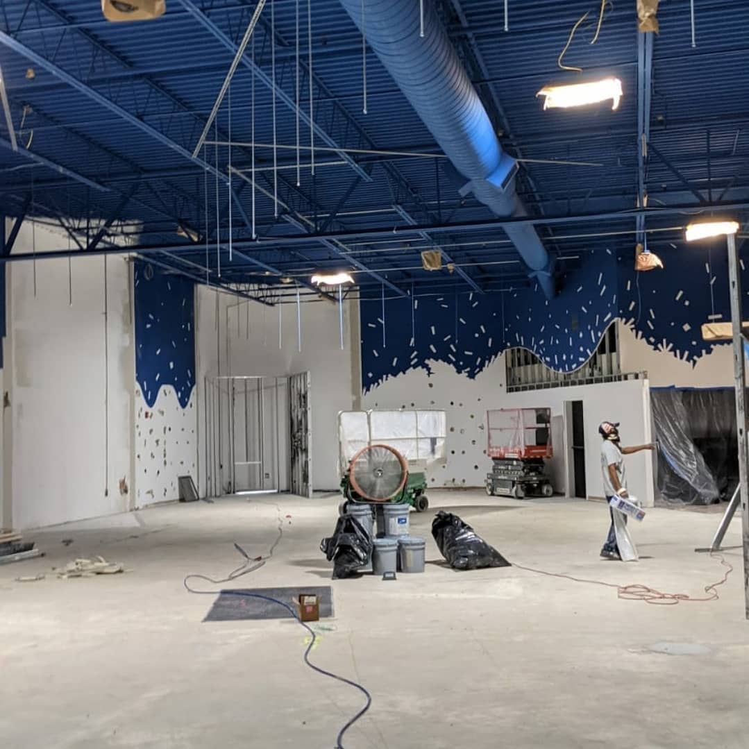 Interior construction: blue ceiling, white walls, person painting, debris on floor.