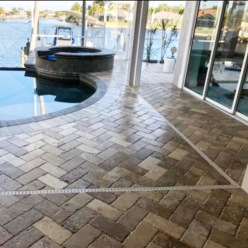 Brick patio with pool, jacuzzi, and water view, with a herringbone pattern.