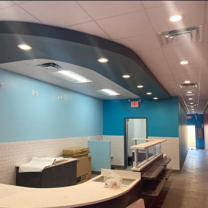 An empty restaurant interior with blue and white walls, counter, recessed lighting, and an exit sign.