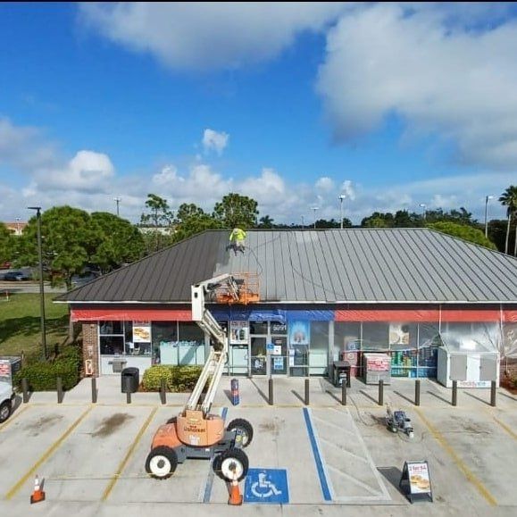 Workers cleaning a commercial building roof with a lift under a blue sky.