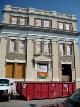 Building under renovation with covered windows, red dumpster, and parked vehicles.