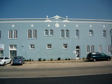 Blue building with arched windows, parked cars, and a clear blue sky.