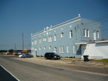 Blue two-story building with white trim on a sunny day. Cars parked on the street in front.