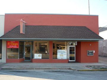 Red storefront with large windows and a brown roof. The business has signs in the windows, and an ATM is on the right side.