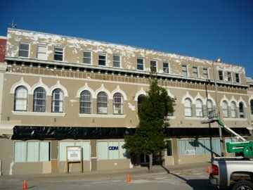 Building exterior, two-story beige facade with arched windows, peeling paint, storefronts covered, blue sky.
