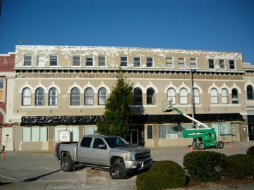 A two-story building with a truck and lift in front, undergoing renovations with peeling paint.