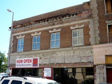 Two-story brick building with missing roof sections, banner reads