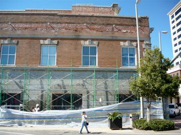 Building under renovation with scaffolding, person walking past.