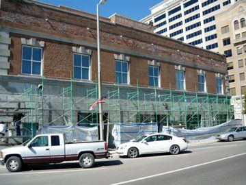 Building under renovation with scaffolding; cars parked on street; brick and stone facade.