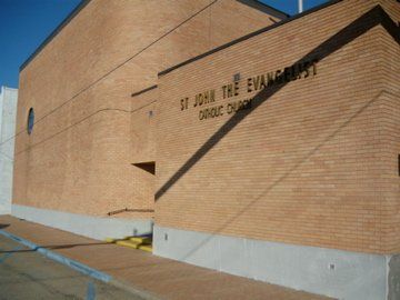Exterior view of St. John the Evangelist Catholic Church, brick building with sign in font against a clear blue sky.
