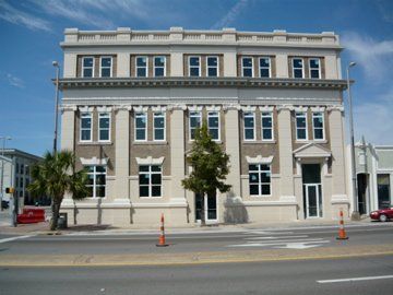 Beige building with many windows on a city street under a blue sky.