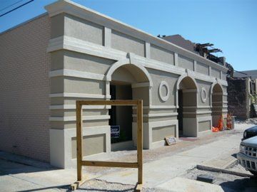 Building exterior with beige and cream facade. Arches, columns, and a wooden barrier are in front.