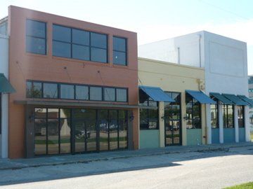 Row of colorful commercial buildings; orange, yellow, and blue facades with large windows and awnings, on a sunny day.