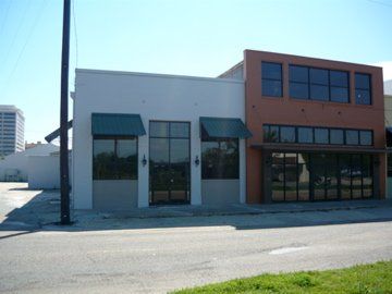 Two-story commercial building: white facade with green awnings, orange section with windows. Empty street.