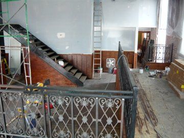 Interior shot of a building under construction. Staircase and balcony with ornate railing are visible.