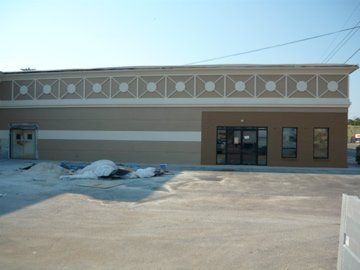 Exterior of a tan building with brown trim, a large glass front door, and an empty parking lot.