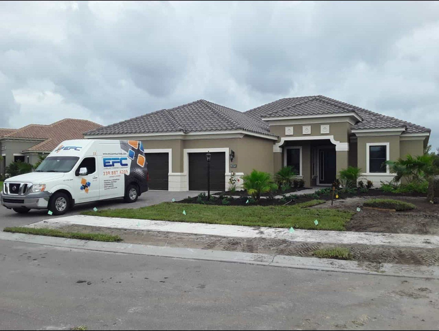 White van parked in front of a beige house with a dark roof and a two-car garage. Overcast day.