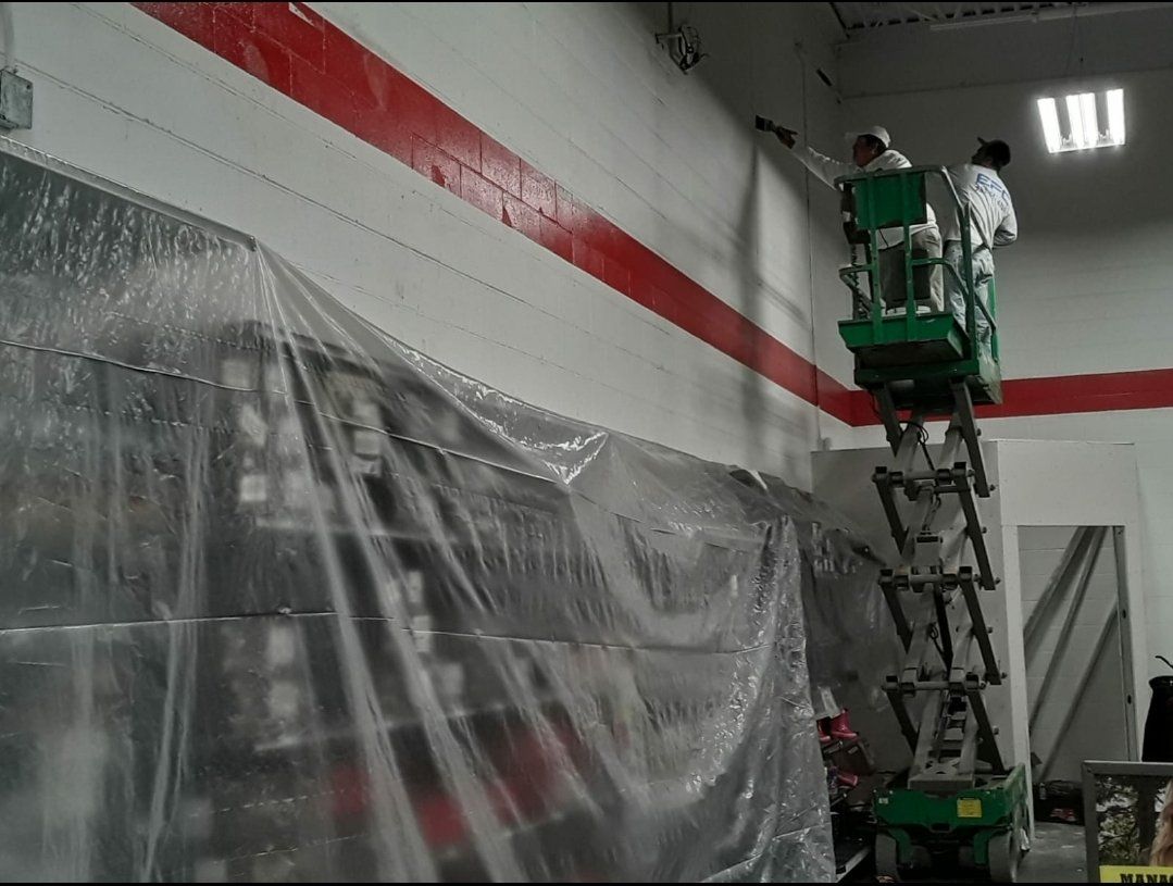 Two painters on lift, painting red stripe on white wall. Plastic protects the lower wall.