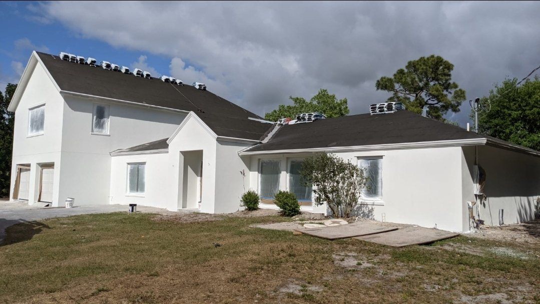 White house with dark roof under a cloudy sky. Construction visible, grass in the foreground.
