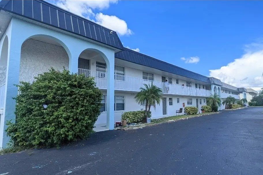 Apartment building exterior with light blue accents, white walls, and black asphalt.