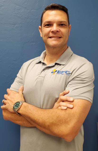 Man in gray polo shirt with arms crossed, smiling, on blue background.