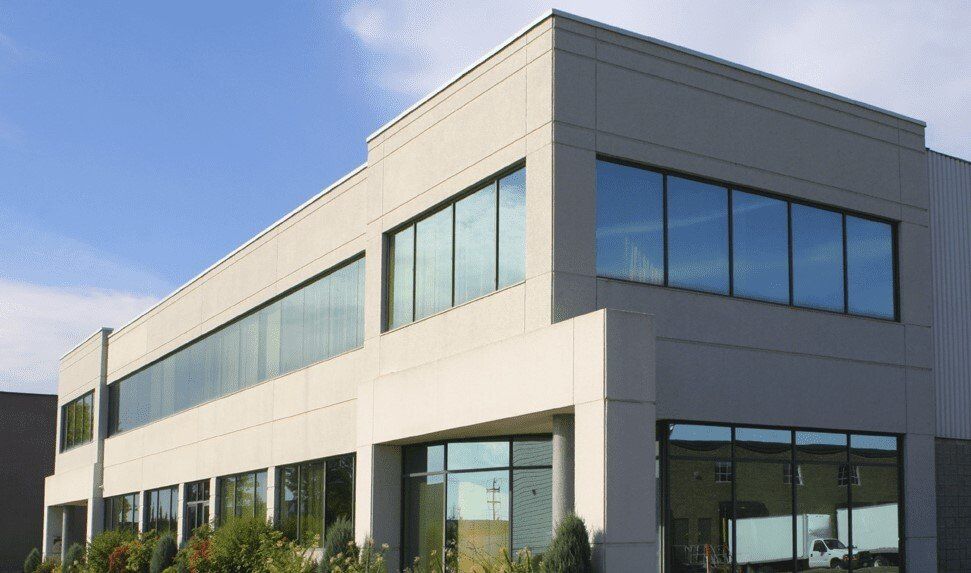 Modern two-story building with large windows reflecting the sky. Beige exterior, sunny day.