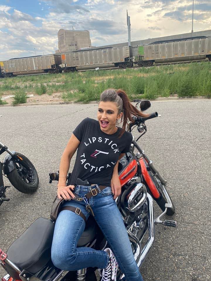 Amanda Hardin on a motorcycle, smiling and wearing a Lipstick Tactical shirt and jeans.
