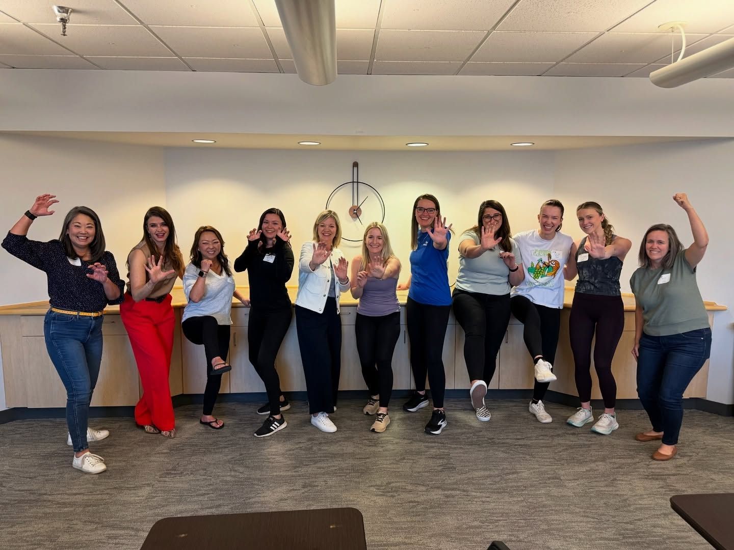 A group of women standing together indoors, smiling and posing confidently with open hands or strong gestures