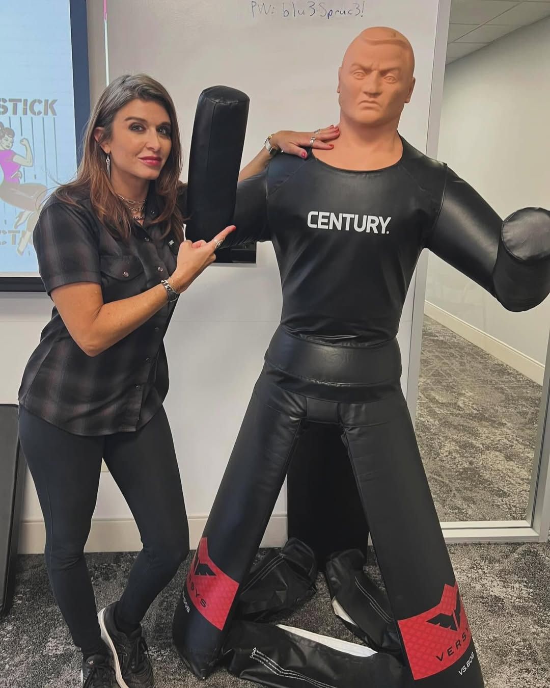 Amanda Hardin holding a rifle indoors, standing in front of Route 66 wall artwork.