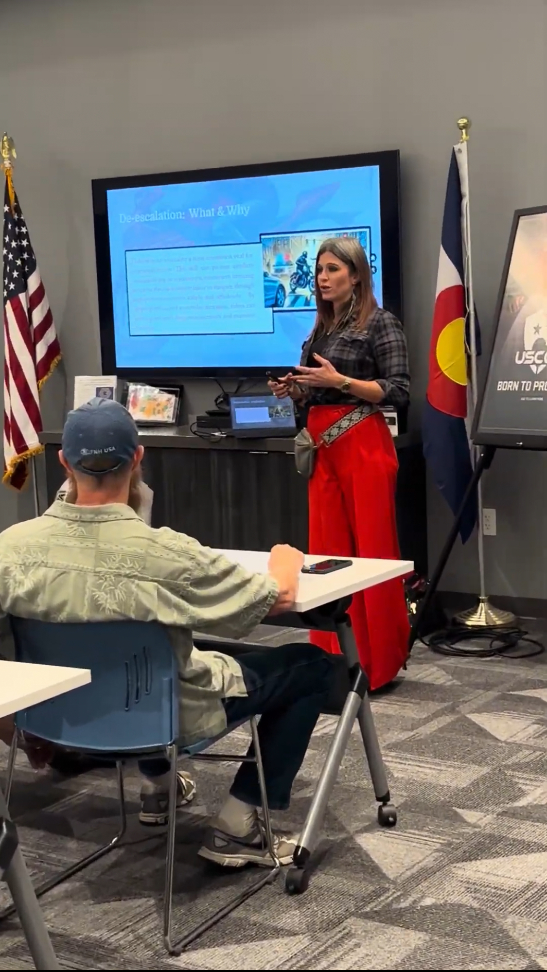 Amanda Hardin seated in office holding a custom-painted rifle, smiling confidently at the camera.