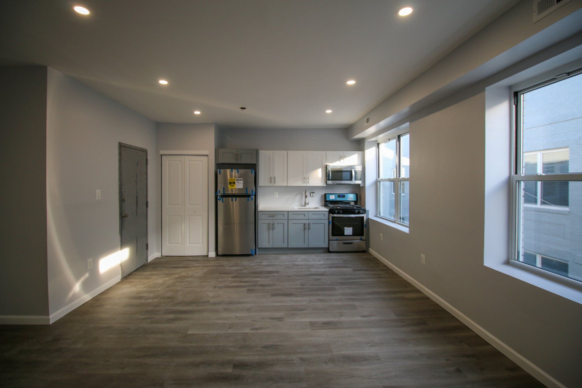 Updated unit with grey flooring and white kitchen with stainless steel refrigerator.