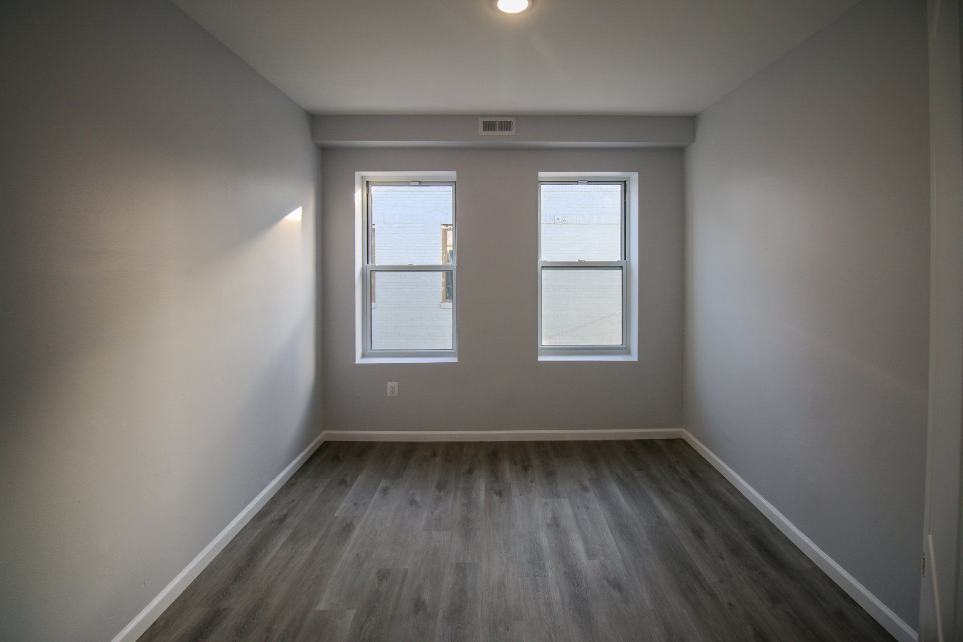 Updated bedroom with grey flooring and two windows.